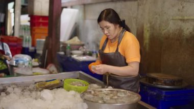 Yaşlı Asyalı kadın Tayland 'ın Bangkok kentindeki yerel bir pazarda müşteriye satmak için karides hazırlıyor.
