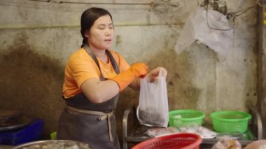 Tayland 'ın Bangkok kentindeki bir balık pazarında müşteriyi teslim etmek için plastik poşette balık hazırlayan Asyalı bir işçi.