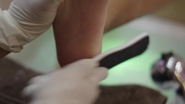 Macro close up shop of a pedicure expert hand filing a left foot in a nail salon - Health concept