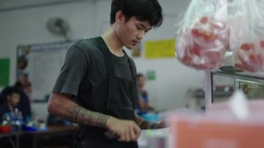 Tayland, Bangkok 'ta yemek hazırlamak için yemek kesen sokak yemekleri satan genç bir satıcı.