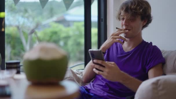 Młody Człowiek Oglądając Serię Swoim Smartfonie Podczas Palenia Jointa Nowa — Wideo stockowe