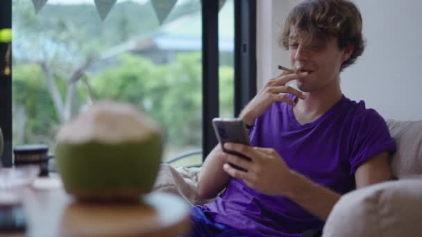 Ung Man Tittar Serien Sin Smarta Telefon Medan Röker Joint — Stockvideo