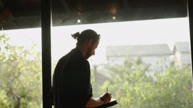 Uzun boylu, at kuyruklu bir adam tabletine bir şey çiziyor.