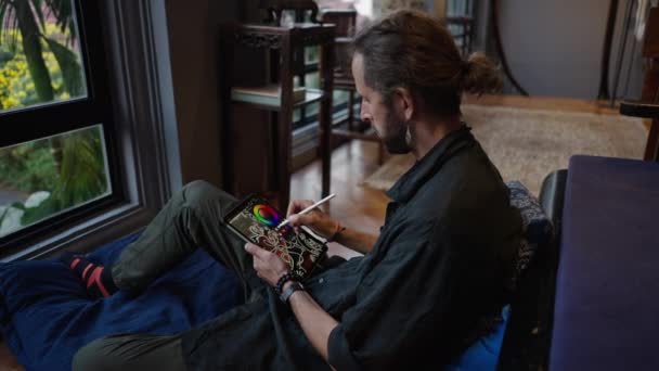 Dunne Boheemse Jongen Tekent Iets Zijn Tablet Tijdens Het Zitten — Stockvideo
