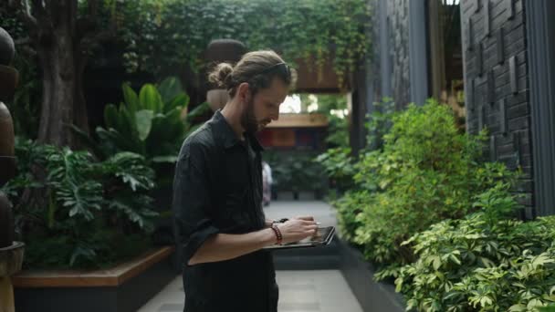 庭で彼のタブレットに何かを描く白人男性 オンラインワーカー — ストック動画