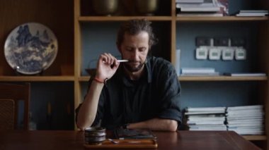 Siyah tişörtlü, kahvesini yudumlayan ve tabletine bakan yetişkin bir adam.
