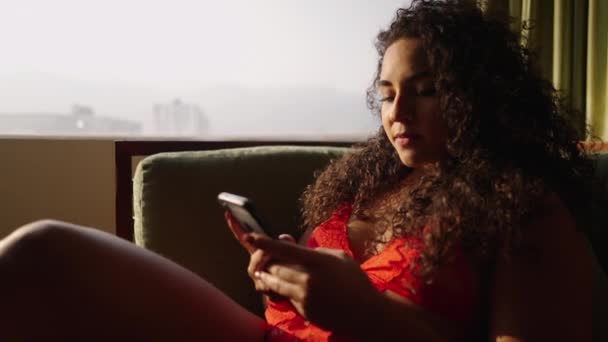 ブルネットの女の子は晴れた窓で彼女の携帯電話上でテキストメッセージ ボディポジティブ — ストック動画