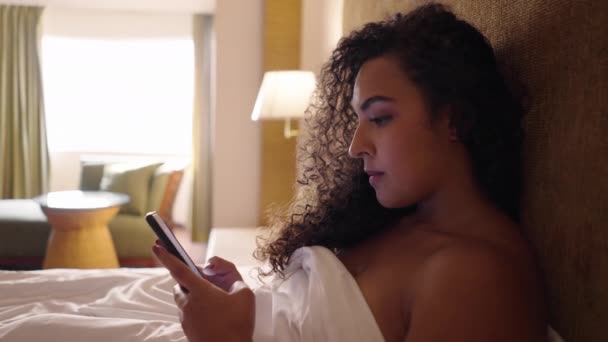 髪の毛の女性は彼女のベッドの上に横たわっている彼女の電話でチャット ボディポジティブ — ストック動画