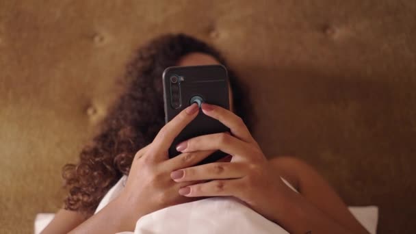 智能手机是由一个无法辨认的女人在床上发短信的 身体呈阳性 — 图库视频影像