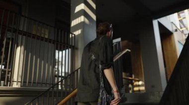 Sakallı beyaz çocuk fil çantasıyla merdivenlerden çıkıyor.