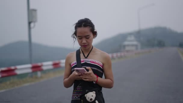 女の子は山の道で彼女の携帯電話を見る ワンダラー — ストック動画
