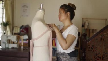 Taylandlı bir kadın stüdyosundaki bir mankenin elbisesini düzeltiyor.