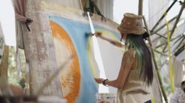 Sırtı dönük bir kadın ressam fırçayla tuvale resim yapan bir şapka takıyor - hippi sanatçı