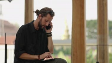 Sakallı tasarımcı telefonda konuşurken tabletine dokunuyor.