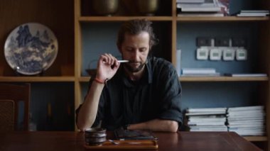 Siyah tişörtlü, kahvesini yudumlayan ve tabletine bakan yetişkin bir adam.