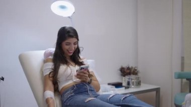 Güzel bir hasta koluna sargılı bir şekilde telefonuna bakar. 4K yatay hat ile.