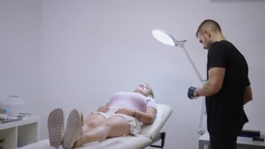 Sarışın hasta uzanıp doktordan anestezi kremi alıyor.