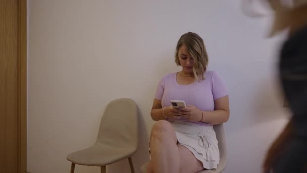 Twee Meisjes Kijken Naar Hun Mobiele Telefoon Een Wachtkamer Kliniek — Stockvideo