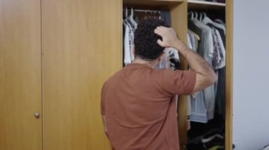 Kaslı Latin adam gardırobunu açıyor ve kıyafetlere bakıyor - 4K Yatay Video