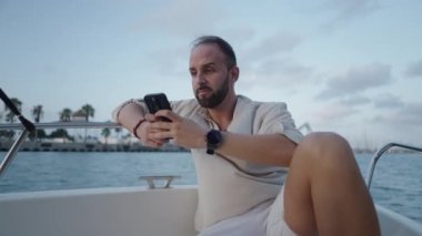 Avrupalı bir adam yelken açarken telefonuna bakıyor.