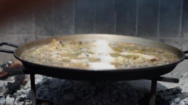 Yetişkin bir el, geleneksel İspanyol yemekleri olan paella tavasında pirinç karıştırır.