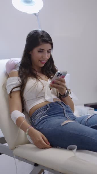 彼女の携帯電話を見て面白いものを見ている間ストレッチャー上の白人患者 Fhd垂直ビデオ — ストック動画