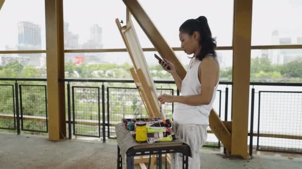 Una Mujer Asiática Mira Teléfono Móvil Junto Sus Herramientas Pintura — Vídeo de stock