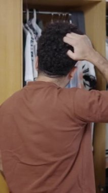 Kaslı latin adam gardırobunu açıyor ve kıyafetlere bakıyor.