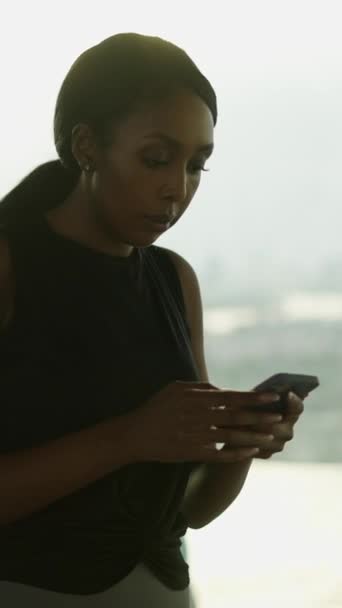 背景に無限のプールを持つ彼女の携帯電話を使用するアフリカの女性 ゴールデンアワー ライフスタイルのコンセプト Fhd 垂直ビデオ — ストック動画