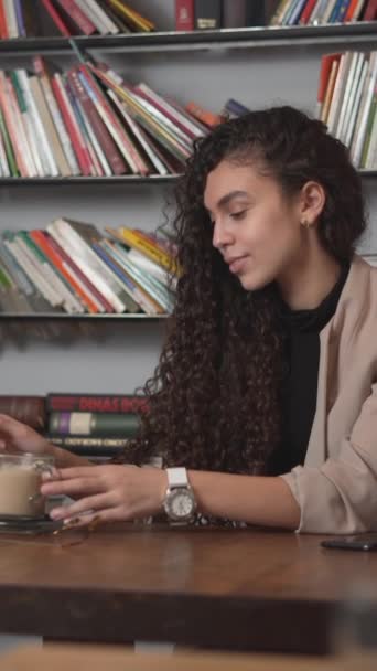 Кудрявая Женщина Сидит Библиотеке Перемешивает Чашку Кофе Пьет Средний Выстрел — стоковое видео