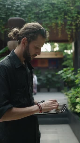 庭で彼のタブレットに何かを描画する白人男性 Fhd垂直ビデオ — ストック動画
