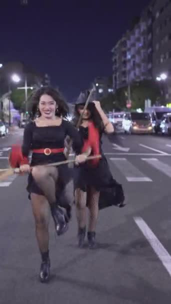 美丽的女人穿着女巫服装在街上嬉笑 玩巫术扫帚 晚上去参加万圣节派对 后撤弹射 垂直1080 — 图库视频影像