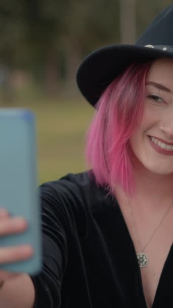 漂亮的女孩 一头粉红的头发 戴着黑色的帽子 在手机上摆出一副自拍的样子 慢动作 垂直1080视频 — 图库视频影像