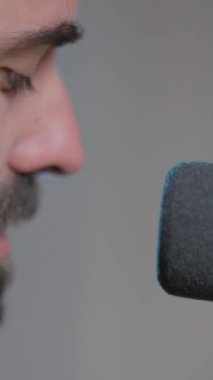 Genç sakallı adam mikrofonuna çok yakın şarkı söylüyor.