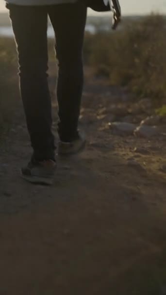 手でギターを保持し 日没に対して田舎のトレイルを歩いている男 バックビュー 垂直フルHdビデオ — ストック動画