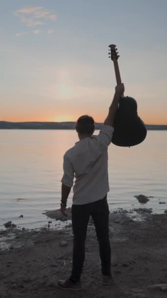 Homem Silhueta Segurando Uma Guitarra Levantada Enquanto Assiste Deslumbrante Pôr — Vídeo de Stock