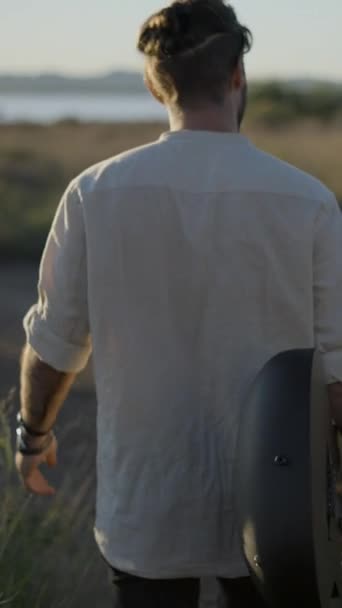 Back Hipster Man Holding Guitar Walking Grassy Field Sunset Shot — Stock video