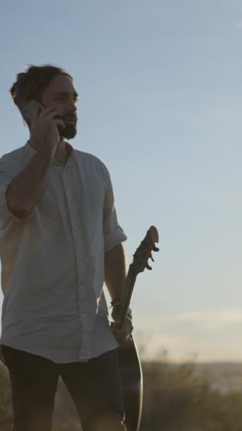Чоловік Стоїть Гітарою Руці Розмовляє Телефону Заході Сонця Вертикальне Fullhd — стокове відео