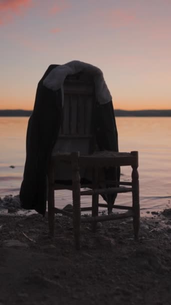 カラフルな日没の湖でジャケットを吊るす木製の椅子のシルエット ジンバルプルバック 垂直フルHdビデオ — ストック動画