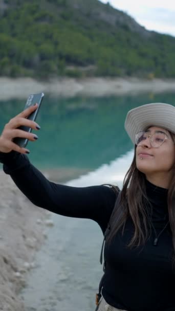 Şapkalı Gözlüklü Genç Kadın Gölün Kenarında Telefonla Selfie Çekiyor — Stok video