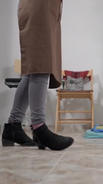 バックグラウンドの床に横たわるペット犬と一緒に働くブラウンエプロンで女性起業家のクロップ画像 中型ショットフルHd垂直ビデオ — ストック動画