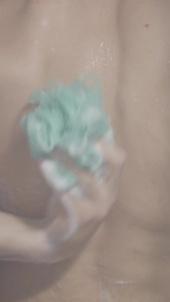 若い白髪の長髪の男は バスタブスポンジでシャワーで彼の背中と胸をこすって 閉じるショット 垂直ビデオ — ストック動画
