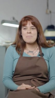 Kahverengi önlüklü esnaf atölyesinde röportaj yapıyor. Ortam görüntüsü FullHD Dikey video