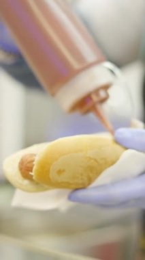 Valencia Caddesi 'ndeki bir panayırda sosisli sandviçin içinde plastik şişeden ketçap sıkan sosisli sandviç hazırlayan kadının elleri.