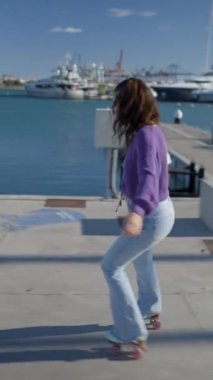 Genç kadın gün ışığında limandaki teknelerle geriye doğru kayıyor - FullHD dikey video