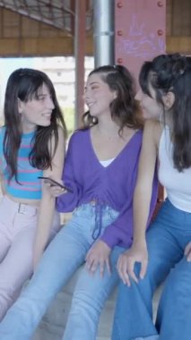 Üç siyah saçlı kız dışarıda telefon kullanırken oturup gülüyorlar, Slomo - FullHD dikey video