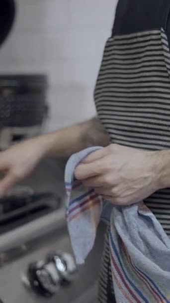 エプロンを着用したタトゥー付き男性シェフは レストランのキッチンで動作します 顔なし Fullhd垂直ビデオ — ストック動画