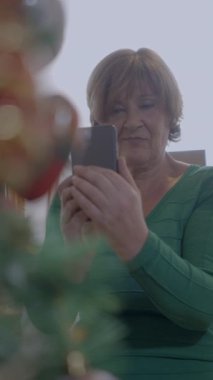 Kadın Emekliler Evi 'nde cep telefonu kamerasıyla parıldayan Noel ağacının fotoğrafını çekiyor. Eğil - Dikey FullHD video