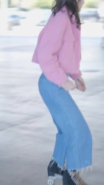 Koyu renk saçlı, kot pantolonlu, pembe ceketli, paten kayan, yakın Slomo, FullHD dikey video.