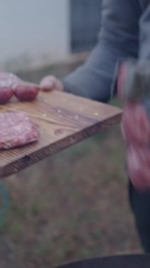 Tanınmayan adam, arkadaşlara yemek yapmak için sosisleri ahşap barbeküye koyuyor.